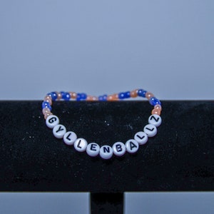 May include: A white beaded bracelet with the word "GYLLENBALLZ" spelled out in black letters.