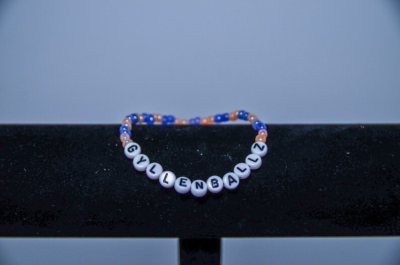 May include: A white beaded bracelet with the word "GYLLENBALLZ" spelled out in black letters.