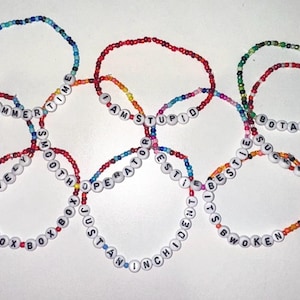 Könnte beinhalten: Ein Set aus acht bunten Perlenarmbändern mit verschiedenen Sätzen, die auf weißen Perlen geschrieben sind. Die Sätze lauten "It's Hammer Time", "Simply Lovely", "Smooth Operator", "I Am Stupid", "Best Friends", "I'm The Best", "B.O.X.B.O.X" und "Botass My Balls Mate".