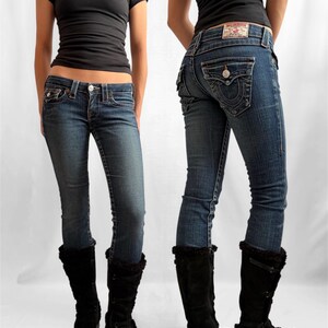 May include: A pair of True Religion blue denim jeans with a button and zipper closure, and a True Religion label on the back pocket. The jeans are paired with a black short-sleeve top and black suede boots.