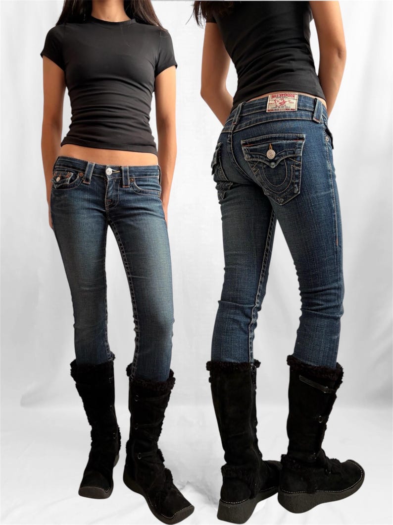 May include: A pair of True Religion blue denim jeans with a button and zipper closure, and a True Religion label on the back pocket. The jeans are paired with a black short-sleeve top and black suede boots.