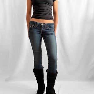 May include: A black short-sleeved t-shirt and blue denim jeans are worn with black knee-high boots. The jeans have a faded wash and a low-rise fit. The boots have a fur trim.