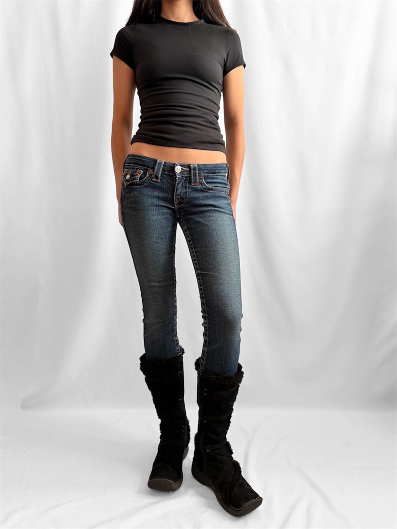 May include: A black short-sleeved t-shirt and blue denim jeans are worn with black knee-high boots. The jeans have a faded wash and a low-rise fit. The boots have a fur trim.