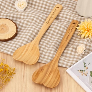 May include: Two wooden heart-shaped kitchen spatulas with the words "Spooning Forever" and "Lucas & Sonia" engraved on them.
