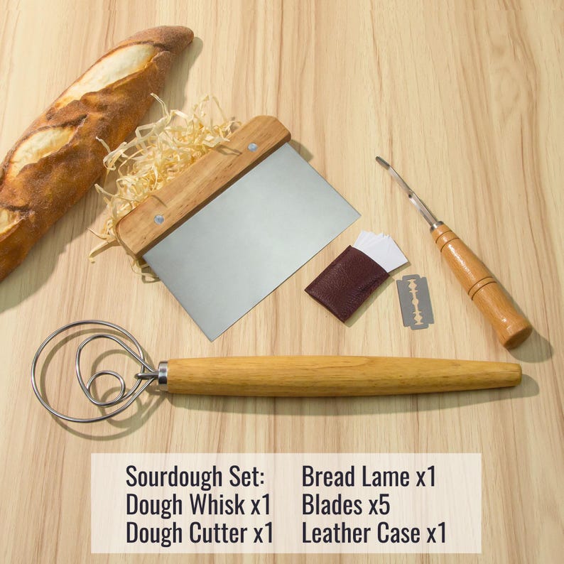 May include: A sourdough baking set with a wooden dough whisk, a dough cutter, a bread lame with a leather case and five blades. The set is on a wooden surface with a loaf of bread and wood shavings.