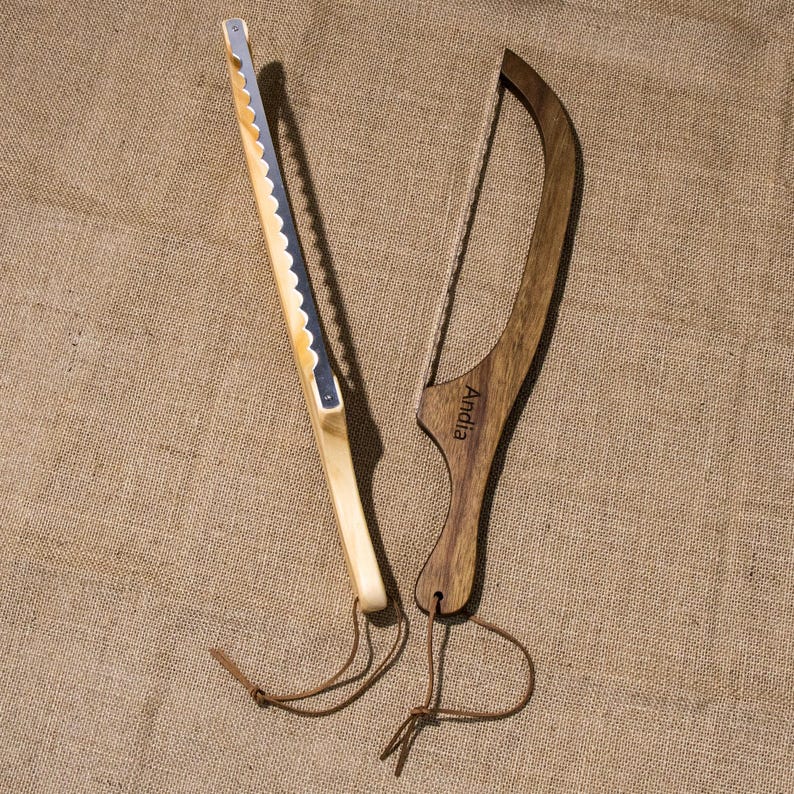 Puede incluir: Dos cuchillos de pan de madera con correas de cuero. Un cuchillo tiene una hoja dentada y el otro un alambre. El cuchillo con el alambre tiene la palabra "Andia" grabada en el mango.