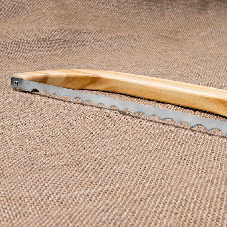 Puede incluir: Un cuchillo para pan con mango de madera y hoja dentada. El cuchillo est&aacute; sobre una superficie de arpillera marr&oacute;n.