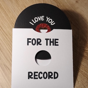 Puede incluir: Tarjeta de felicitaci&oacute;n hecha a mano con un dise&ntilde;o de disco de vinilo negro. La tarjeta dice "I LOVE YOU" encima de un coraz&oacute;n rojo con purpurina y "FOR THE RECORD" debajo. La tarjeta es blanca con un recorte circular.