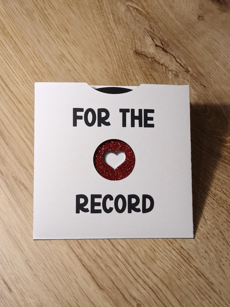 Puede incluir: Una tarjeta blanca con el texto "FOR THE RECORD" en negro. Una forma de coraz&oacute;n con purpurina roja est&aacute; recortada de la tarjeta. La tarjeta est&aacute; sobre una superficie de madera.