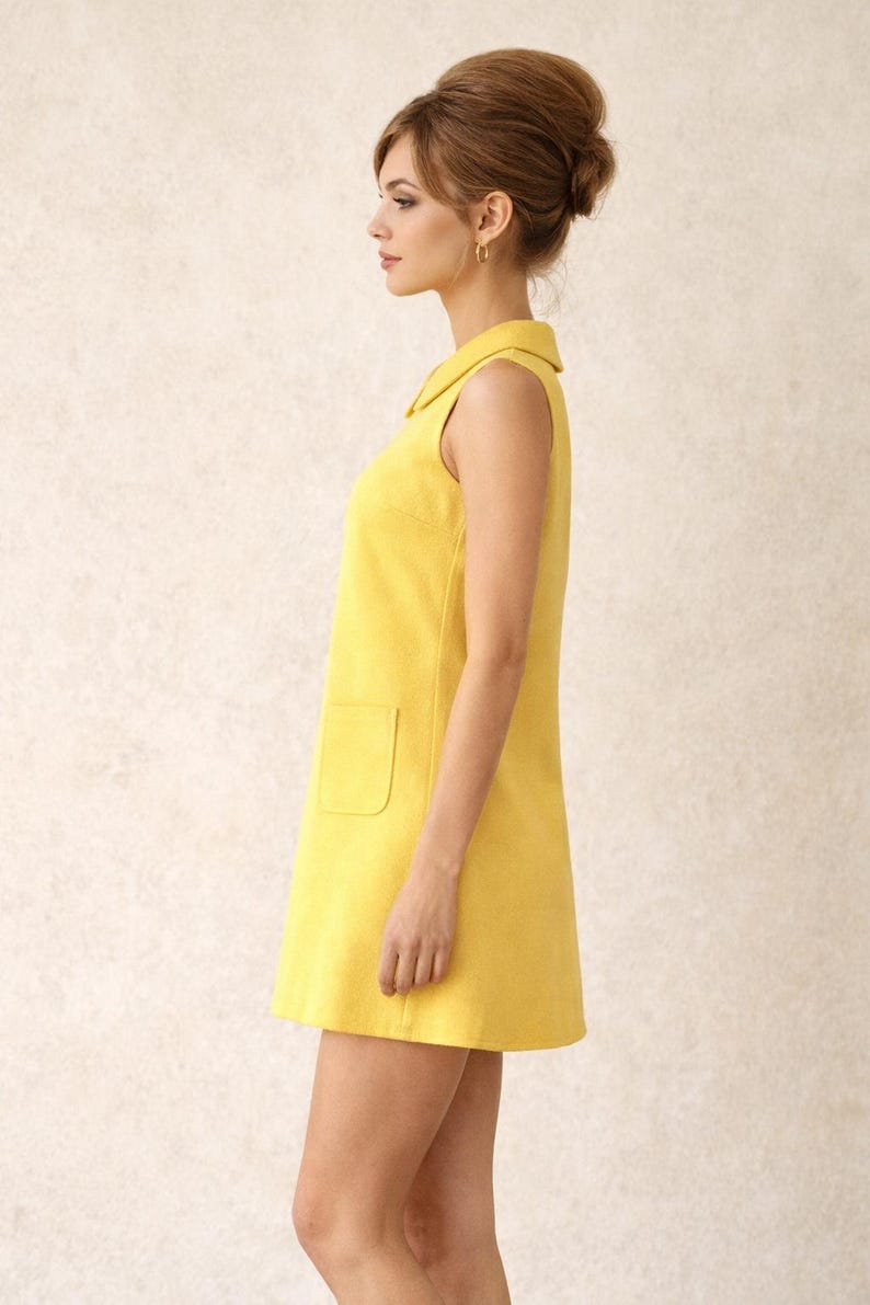 May include: A sleeveless, yellow dress with a collared neckline and a single front pocket. The dress has a simple, A-line silhouette, and is made of a textured fabric. The dress is knee-length.