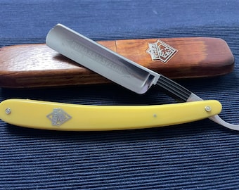 May include: A straight razor with a yellow plastic handle and a wooden case. The razor blade is engraved with the text "Solingen B.B.Z. Special" and the case has a logo with the text "Puma".