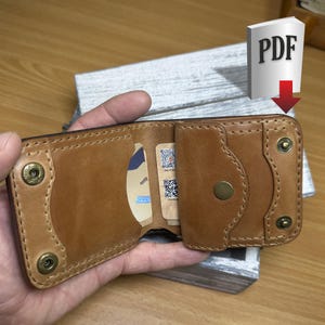 May include: Open, brown leather wallet with card slots and a snap closure. The wallet has brass-colored rivets and a stitched design. The wallet is open, revealing cards inside. The PDF icon is in the background.