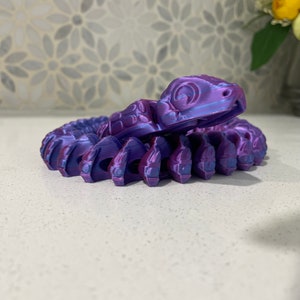 Op de afbeelding: Een 3D-geprint, gesegmenteerd slangbeeldje in paars en blauw. De slang is opgerold met zijn kop omhoog en zijn ogen dicht.