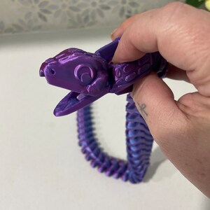 Op de afbeelding: Een 3D-geprint slangen speelgoed in paars en blauw. De slang is gesegmenteerd en heeft een gedetailleerd hoofd met een textuur.