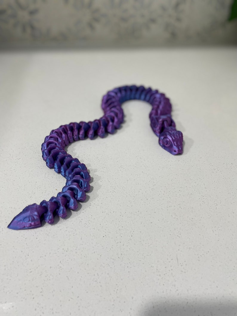 Op de afbeelding: Een paarse en blauwe iriserende plastic slangachtige armband met een gesegmenteerd ontwerp.