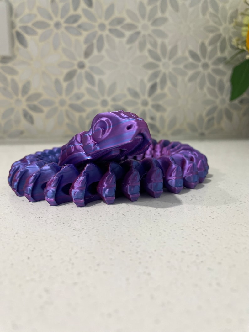 Op de afbeelding: Een 3D-geprint slangbeeldje in paars en blauw met een opgerold lichaam en een opgeheven kop.