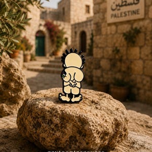 May include: A metal enamel pin featuring a cartoon character with spiky black hair, seen from behind with hands clasped, wearing light-colored clothing. The character has a small flag detail on the arm. The pin has a black outline and base.