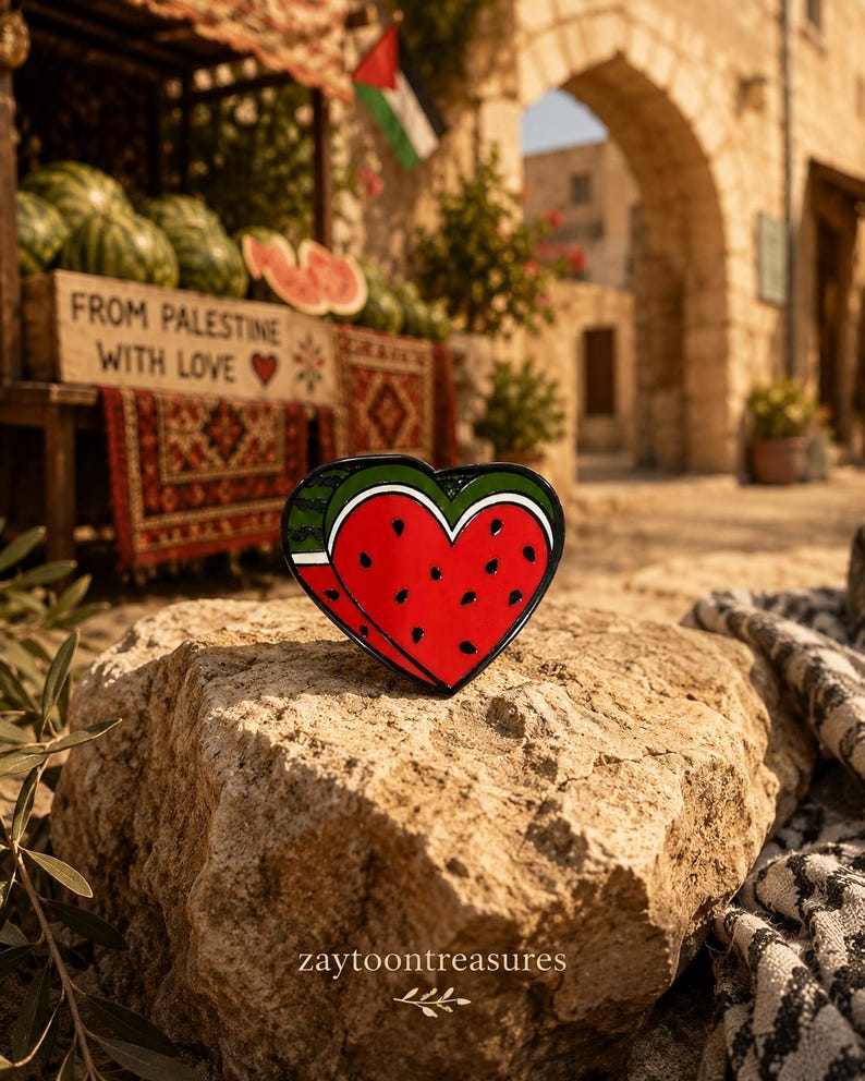 May include: A heart-shaped enamel pin featuring a red watermelon slice with black seeds, a white rind, and a green outer edge. The design is rendered in vibrant colors with a glossy finish, showcasing a stylized fruit motif in a classic heart shape.
