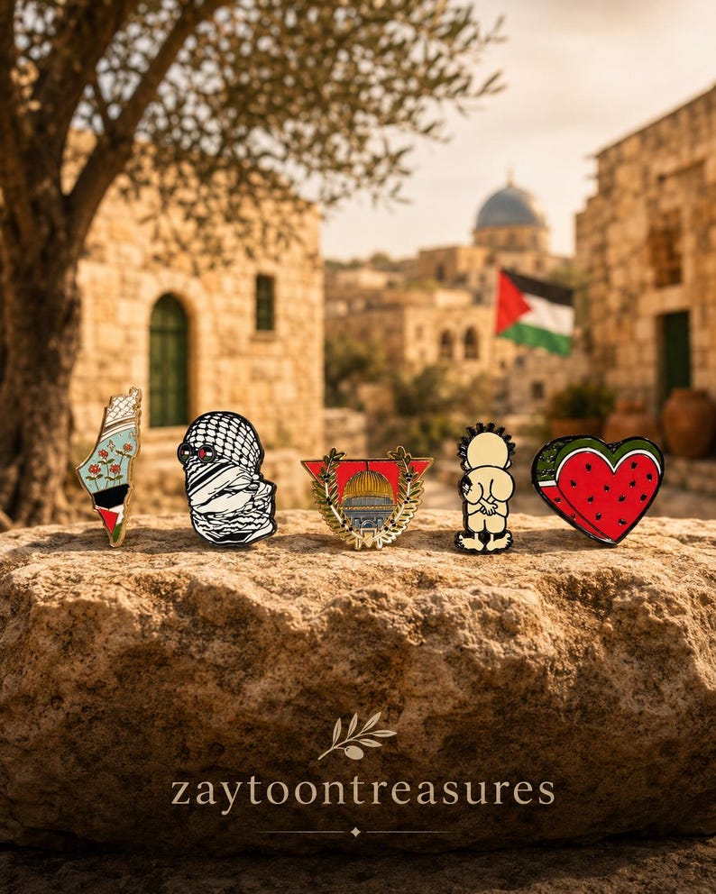 May include: Five enamel pins arranged in a row. The first is a map of Palestine with flowers and flag colors. The second is a keffiyeh-patterned figure. The third is a gold-framed Dome of the Rock. The fourth is a cartoon figure. The fifth is a watermelon heart.