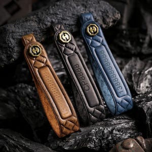 May include: Three leather keychains in brown, black, and blue, each with a quilted pattern and a gold-colored emblem. The brown keychain has the number "1388888888" embossed, the black one has "CP8888", and the blue one has "1388888888".