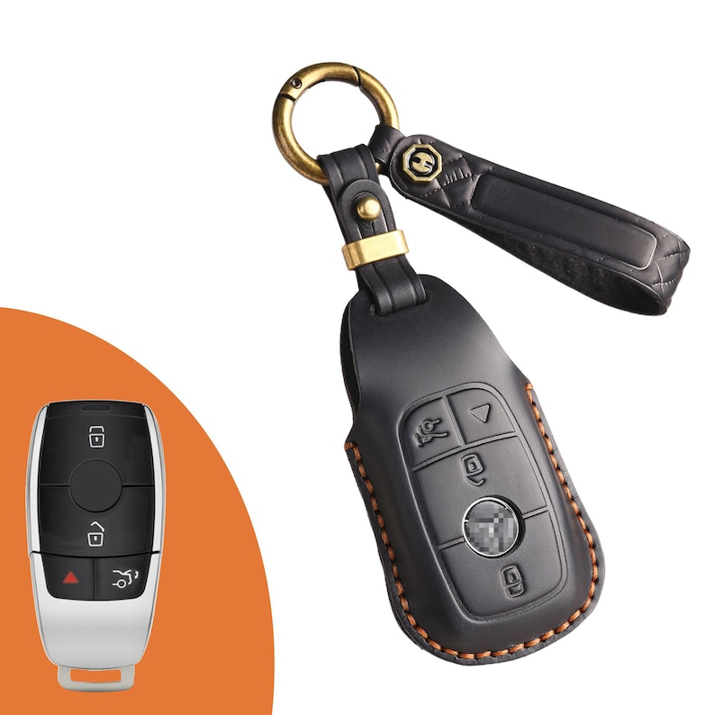 May include: Black leather key fob cover with a gold-colored metal ring and accents. The key fob cover has a stitched brown border and a black leather strap. A car key is shown on the left.