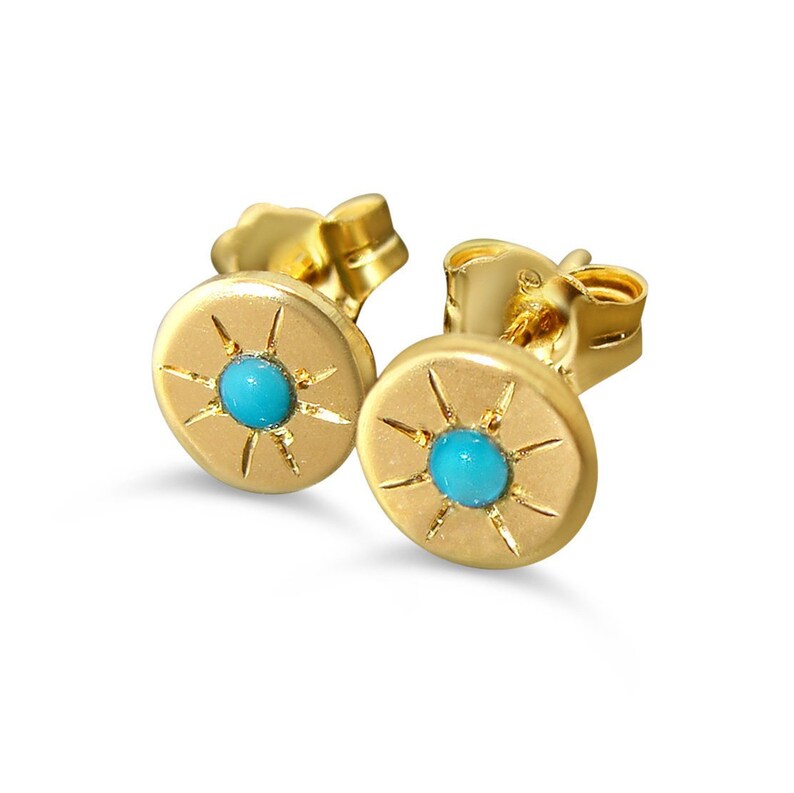 May include: A pair of gold stud earrings with a turquoise stone in the center of each earring. The earrings have a sunburst design around the stone.