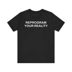 May include: Black t-shirt featuring the white text "REPROGRAM YOUR REALITY". The short-sleeved top has a crew neck. The material looks soft and comfortable. A casual garment for everyday wear.