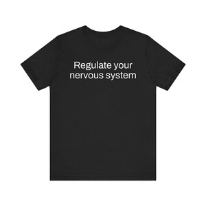 May include: Black t-shirt with the white text "Regulate your nervous system". The short-sleeved shirt is made of a soft material and is suitable for casual wear. The text is centered on the front of the shirt.