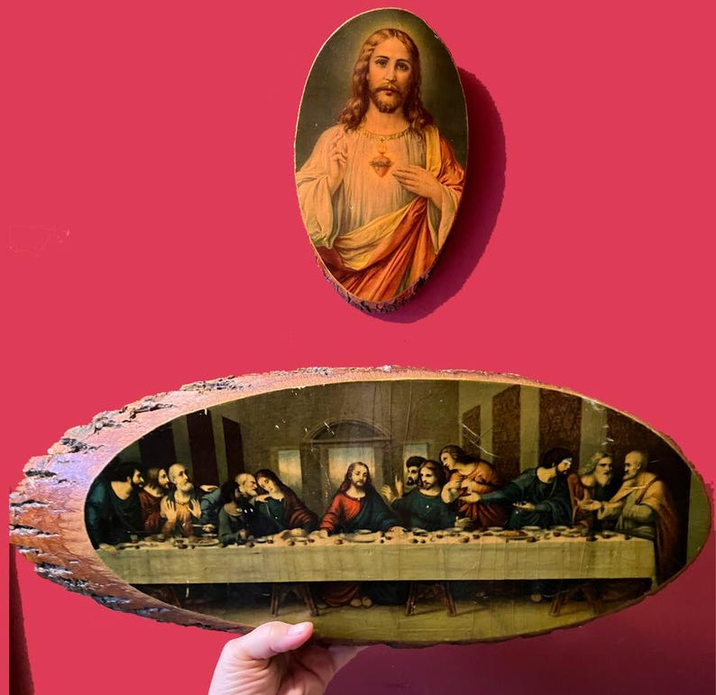 May include: Two religious artworks. The top piece is an oval-shaped portrait of Jesus with a golden halo and a red heart. The bottom piece is a long, irregular-shaped wooden plaque depicting The Last Supper.