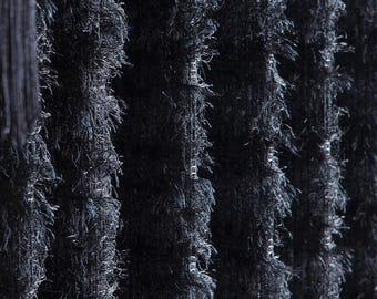 Puede incluir: Primer plano de una tela negra texturizada con líneas verticales. Una pantalla de lámpara roja con flecos negros es visible a la izquierda. La tela tiene una apariencia peluda y con flecos, creando una sensación de profundidad y textura.