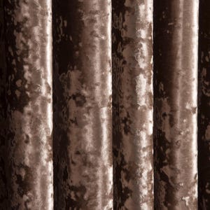 May include: Close-up of a luxurious, textured curtain in a warm, muted brown colour. The fabric has a soft, velvety appearance with subtle variations in tone, creating a rich, elegant look. The vertical folds add depth and dimension.