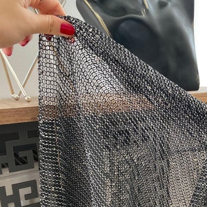 May include: Black mesh fabric with a metallic sheen. The fabric is made of small, interconnected squares.