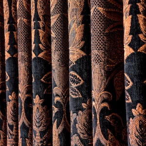 May include: Close-up of elegant, dark blue curtains with a repeating pattern in shades of brown and gold. The design features stylized floral and leaf motifs, creating a luxurious and textured appearance. The curtains are folded in vertical pleats.