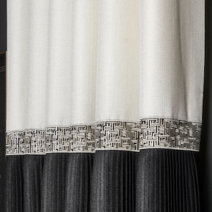 May include: White and black pleated curtains with a geometric pattern trim. The curtains are hung in a room with a dark wall and a framed picture.