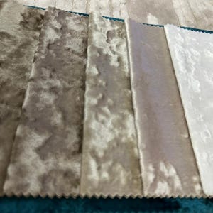 K&ouml;nnte beinhalten: Ein Stoffmusterbuch mit f&uuml;nf rechteckigen Streifen aus Knitter-Samt, die in einem Farbverlauf von Dunkelbraun bis Hellbeige und Wei&szlig; angeordnet sind und an einer dunkelgrauen Kopfleiste mit einem schwarzen Verschluss befestigt sind.
