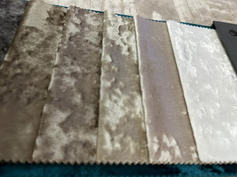 K&ouml;nnte beinhalten: Ein Stoffmusterbuch mit f&uuml;nf rechteckigen Streifen aus Knitter-Samt, die in einem Farbverlauf von Dunkelbraun bis Hellbeige und Wei&szlig; angeordnet sind und an einer dunkelgrauen Kopfleiste mit einem schwarzen Verschluss befestigt sind.
