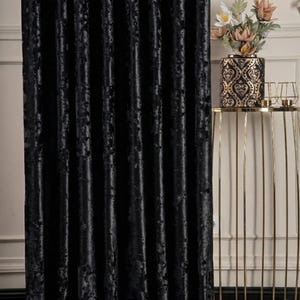 K&ouml;nnte beinhalten: Ein bodenlanger Vorhang aus schwarzem Knitter-Samt mit einer strukturierten, lichtreflektierenden Oberfl&auml;che. Der Stoff f&auml;llt in vertikalen Falten, die eine Reihe tiefer Schatten und Glanzlichter auf dem Material erzeugen und bis zum Boden reichen.