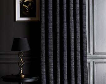 Puede incluir: Cortinas texturizadas de color gris oscuro cuelgan frente a una pared gris oscuro. Una lámpara negra con base dorada se encuentra sobre una mesa auxiliar negra. Una foto enmarcada de un busto está en la pared.