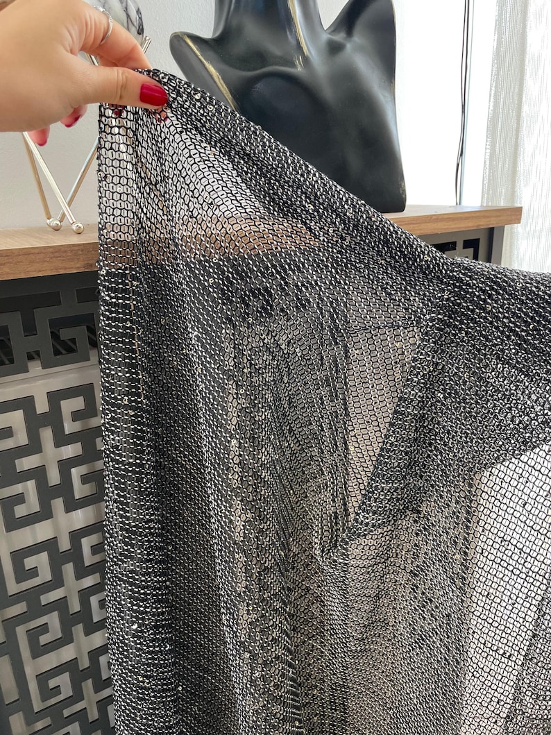 May include: Black mesh fabric with a metallic sheen. The fabric is made of small, interconnected squares.
