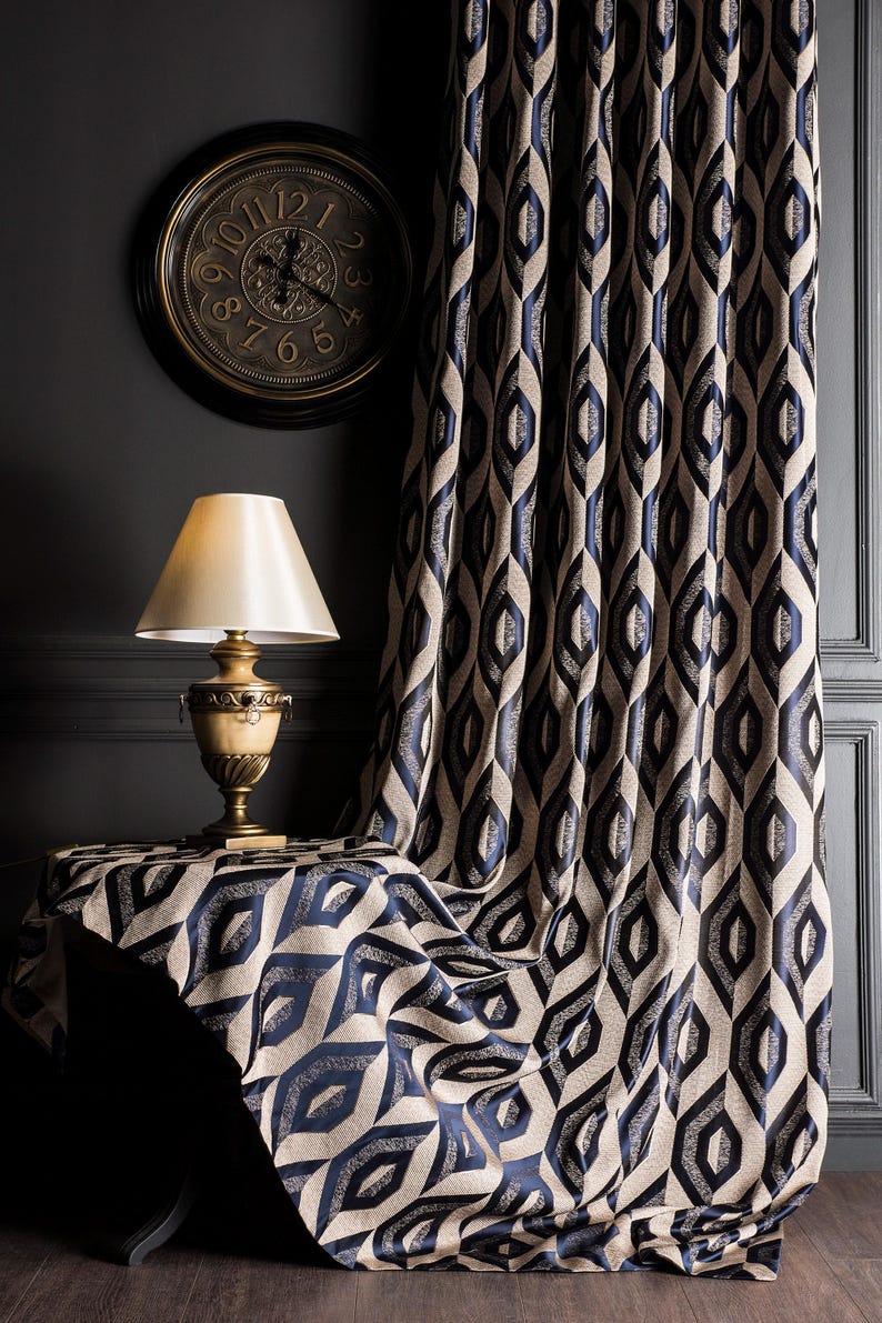 May include: A room interior featuring a patterned curtain, table cloth, and a wall clock. The curtain and table cloth have a repeating geometric design in navy blue and beige. A gold-toned lamp sits on the table. A round clock hangs on the wall.