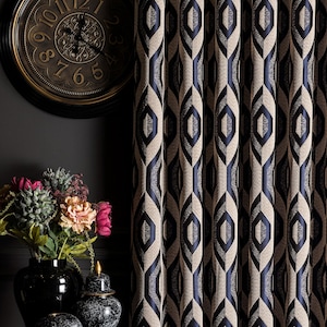 May include: Elegant, patterned curtains in beige and navy blue with a geometric design. A dark, round clock with gold accents hangs on the wall. A black vase holds colorful flowers, adding a touch of vibrancy.