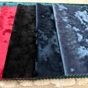 K&ouml;nnte beinhalten: Eine Sammlung von f&uuml;nf rechteckigen Stoffmustern mit einer Knitter-Samt-Textur. Die von links nach rechts gezeigten Farben umfassen Petrol, leuchtendes Rot, sattes Schwarz, tiefes Marineblau und ein helleres, meliertes Blau mit Glanz.