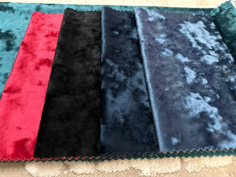 K&ouml;nnte beinhalten: Eine Sammlung von f&uuml;nf rechteckigen Stoffmustern mit einer Knitter-Samt-Textur. Die von links nach rechts gezeigten Farben umfassen Petrol, leuchtendes Rot, sattes Schwarz, tiefes Marineblau und ein helleres, meliertes Blau mit Glanz.