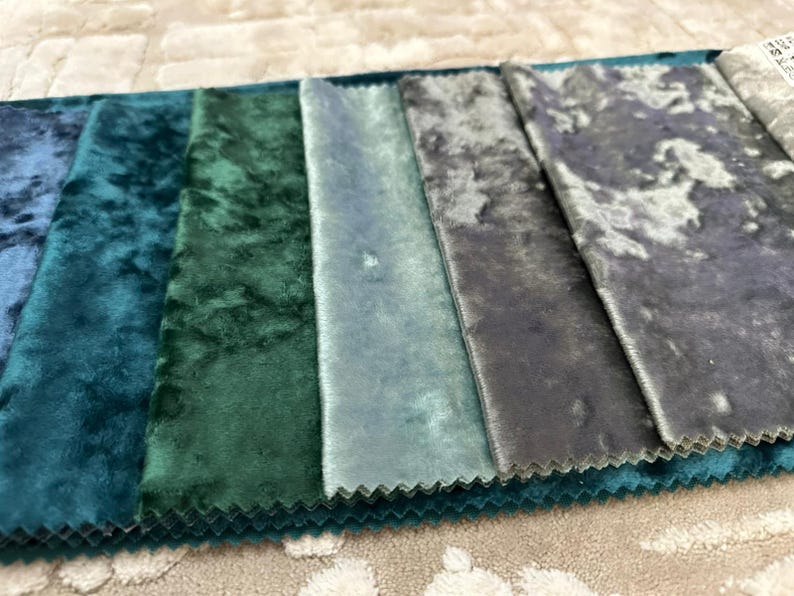 K&ouml;nnte beinhalten: Ein Stoffmusterbuch mit einem Farbverlauf aus zerknitterten Samttexturen in den Farbt&ouml;nen Dunkelblau, Waldgr&uuml;n, Petrol, Hellblau und Anthrazit. Jeder rechteckige Stoffstreifen hat gezackte Kanten und einen ausgepr&auml;gten, reflektierenden Glanz.