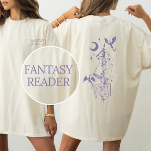 Könnte beinhalten: Ein cremefarbenes T-Shirt mit dem Text "Fantasy Reader" auf der Vorderseite und einer lilafarbenen Illustration eines Schwertes mit Büchern und Drachen auf der Rückseite.