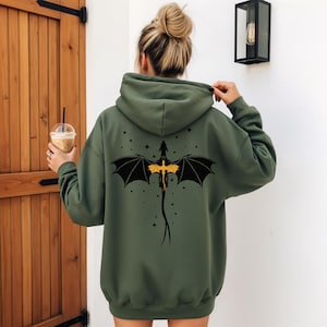 Può includere: Una felpa con cappuccio verde oliva con un disegno di drago nero e giallo sul retro. Il drago ha le ali spiegate ed è circondato da piccole stelle. La felpa ha un cappuccio e maniche lunghe.