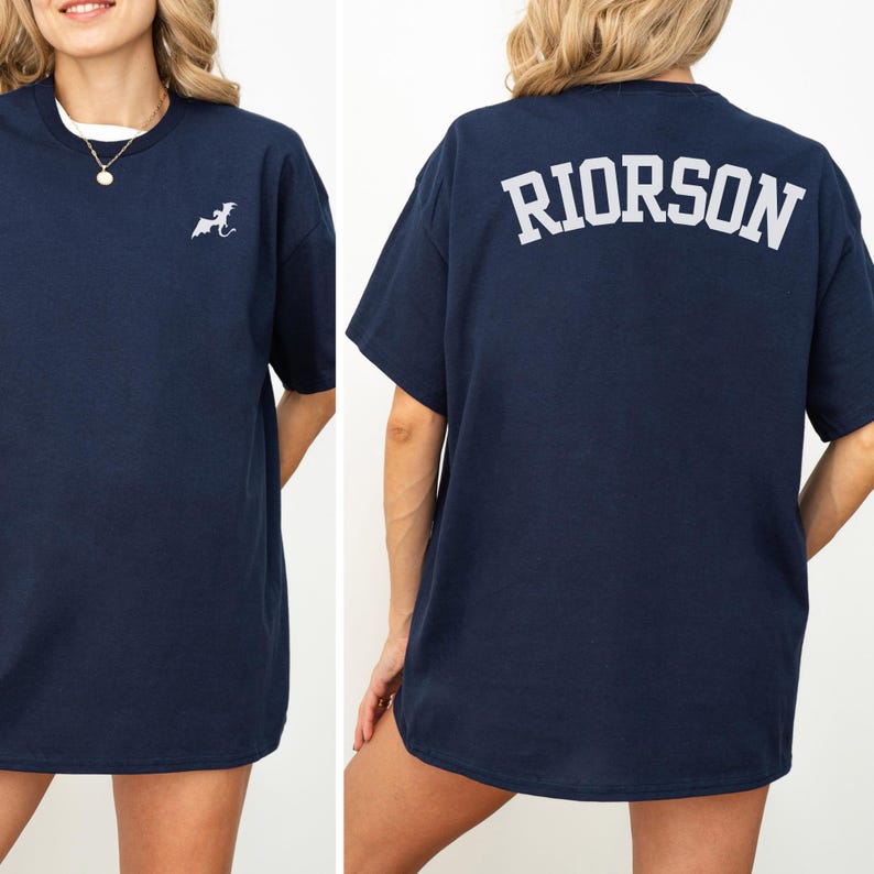 May include: Navy blue t-shirt with a small white graphic on the front and the word "RIORSON" printed in white on the back. The shirt has short sleeves and a crew neck. The model is wearing a white undershirt.
