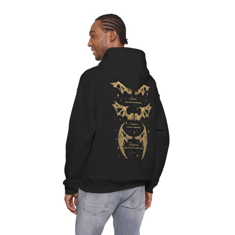 May include: Black hoodie with a gold graphic of three sets of stylized wings and text. The text includes the words "Astral", "Celestial Formations", and "Regina". The hoodie has a hood and a relaxed fit.