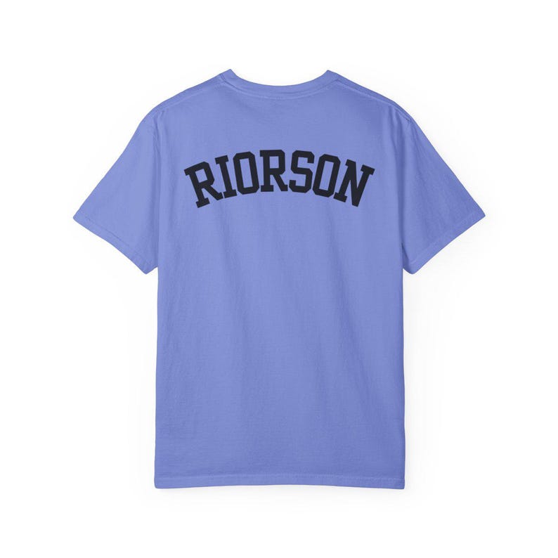 May include: A pale blue t-shirt with the word "RIORSON" printed in black, arched block letters across the back. The shirt has short sleeves and a crew neck. The fabric appears soft.