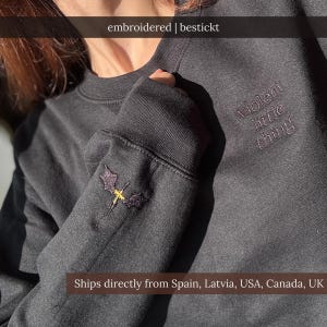 Könnte beinhalten: Dunkelgraues Sweatshirt mit gestickten Details. Der Ärmel zeigt ein kleines Drachendesign in Lila und Gelb. Der Text "violent little thing" ist auf dem Oberarm gestickt. Der Markenname "bestickt" ist ebenfalls sichtbar.